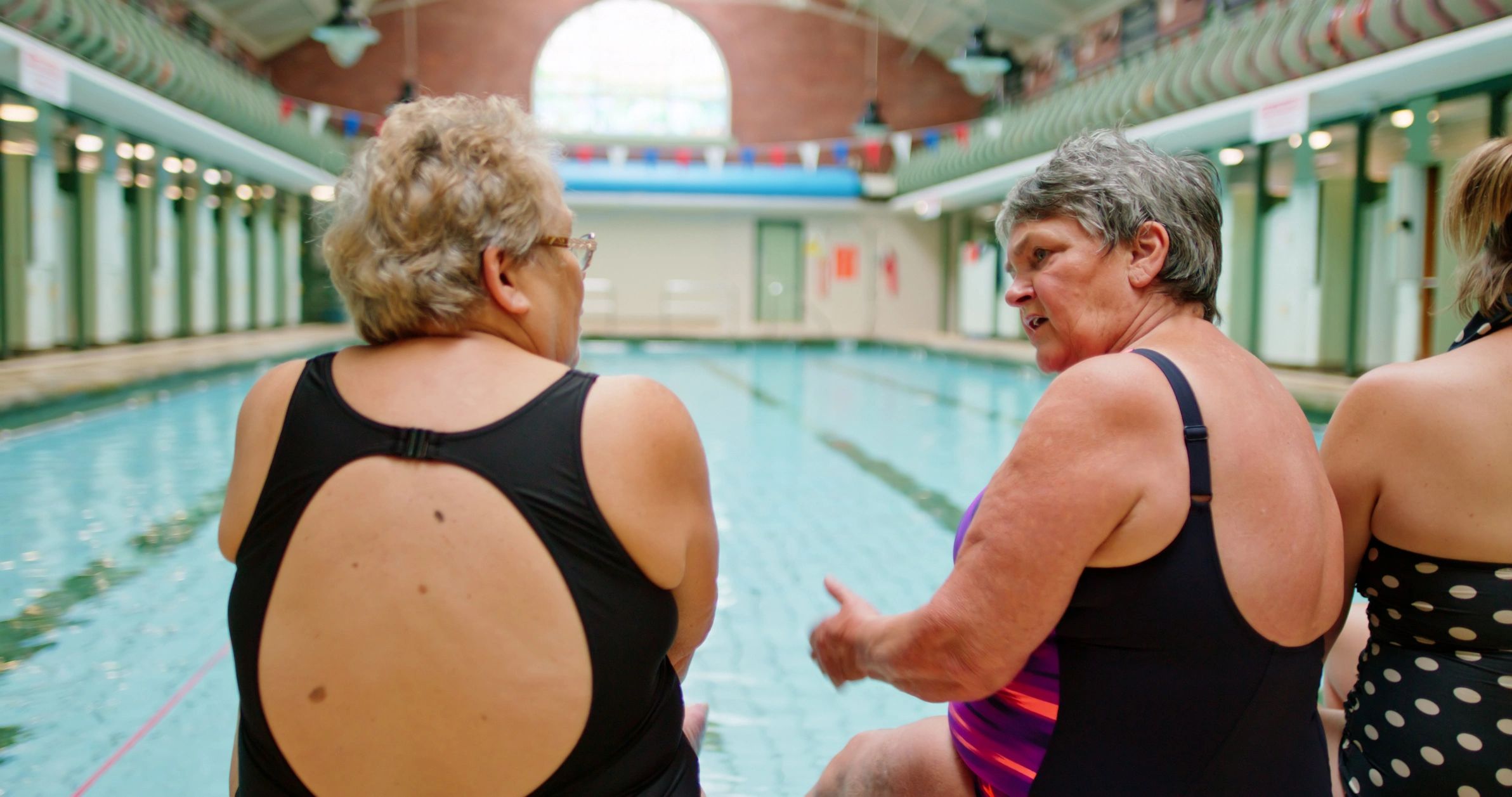 Adults talking at the edge of a swimming pool during instruction